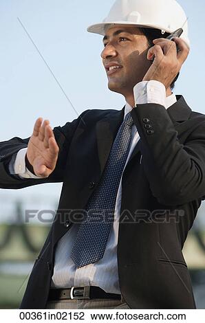 Stock Image - Man with helmet talking on mobile phone and gesturing. Fotosearch