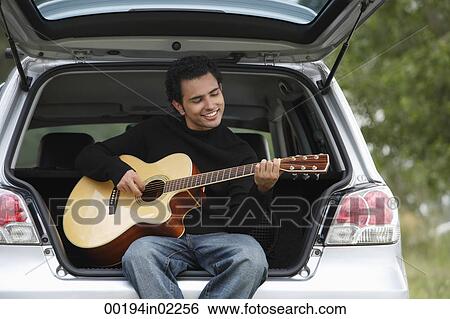 Young man sitting car boot playing guitar View Large Photo Image Stock Photograph - Young man sitting car boot playing guitar. Fotosearch