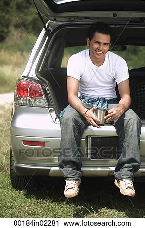 Young man sitting in car boot smiling at camera View Large Photo Image Stock Image - Young man sitting in car boot smiling at camera. Fotosearch