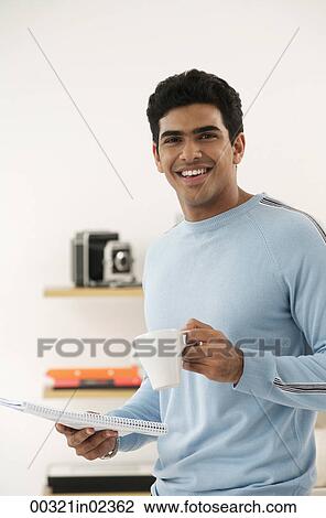 Stock Image - Young man with coffee and paper smiling at camera. Fotosearch