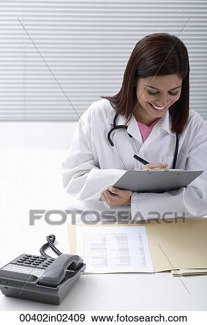 Doctor smiling while writing report View Large Photo Image Stock Photo - Doctor smiling while writing report. Fotosearch