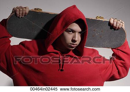 Stock Photography - young man wearing red hooded sweatshirt holding skateboard. Fotosearch