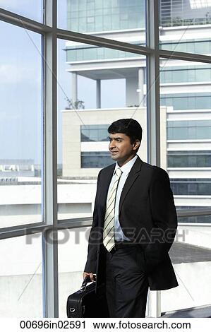 Stock Image - business man holding briefcase, looking out of the window. Fotosearch