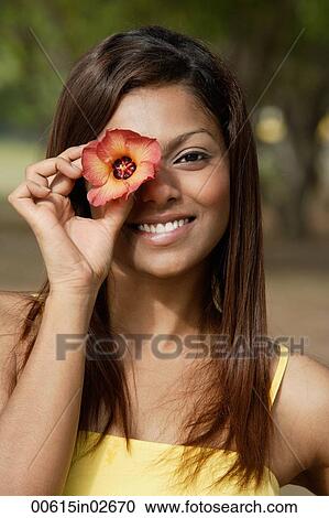 Stock Image - woman covering an eye with flower, smiling. Fotosearch