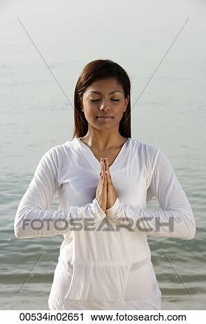 Stock Image - woman practicing yoga on the beach, eyes closed. Fotosearch
