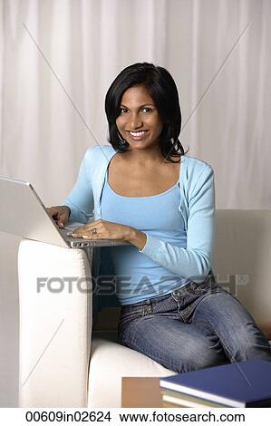 Picture - woman sitting on couch using laptop. Fotosearch