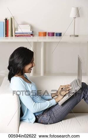 Stock Image - woman sitting on couch, using laptop. Fotosearch