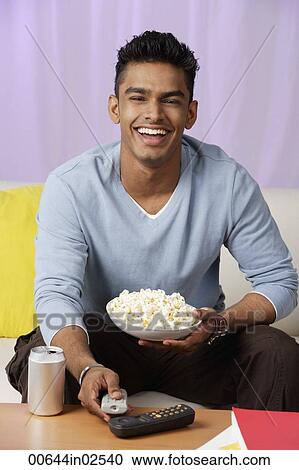 Stock Image - young man holding popcorn in hand, laughing. Fotosearch