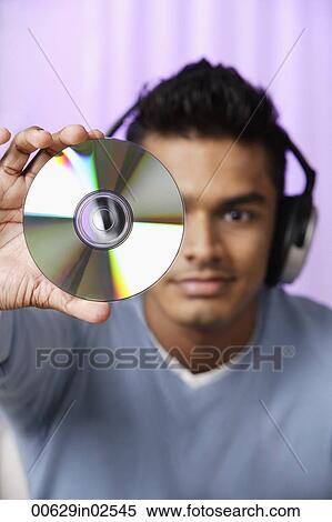young man with headphones on, holding compact disc in front of him View Large Photo Image Stock Photography - young man with headphones on, holding compact disc in front of him. Fotosearch