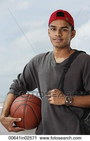 Stock Image - young man with red cap holding basket ball and carrying backpack. Fotosearch