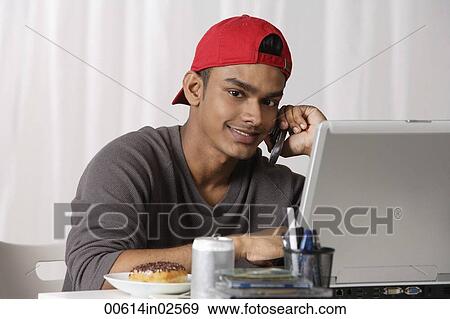 young man with red cap, talking on phone and working on laptop View Large Photo Image Stock Photo - young man with red cap, talking on phone and working on laptop. Fotosearch