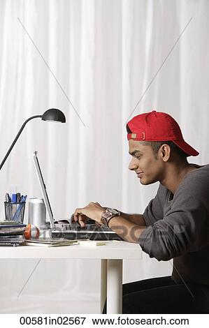 Stock Photo - young man with red cap working on laptop. Fotosearch