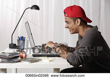 Stock Photograph - young man with red cap working on laptop. Fotosearch