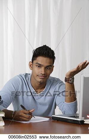 Stock Image - young man writing at his desk, puzzled. Fotosearch