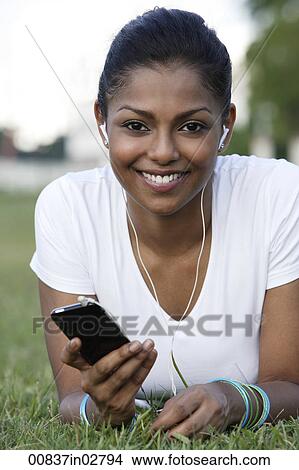 Young woman laying on grass listening to MP3 player View Large Photo Image Picture - Young woman laying on grass listening to MP3 player. Fotosearch