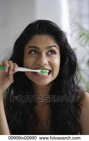 Stock Image - Head shot of Indian woman brushing her teeth and looking up. Fotosearch