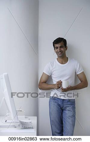 Indian man holding a drink and looking at computer. View Large Photo Image Stock Image - Indian man holding a drink and looking at computer.. Fotosearch