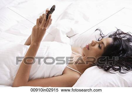 Indian woman laying down in bed looking at phone. View Large Photo Image Stock Photography - Indian woman laying down in bed looking at phone.. Fotosearch