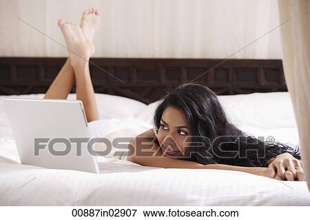 Indian woman laying on bed looking at laptop View Large Photo Image Stock Photo - Indian woman laying on bed looking at laptop. Fotosearch