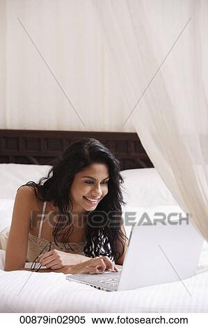 Indian woman laying on bed looking at laptop computer and smiling View Large Photo Image Stock Photography - Indian woman laying on bed looking at laptop computer and smiling. Fotosearch