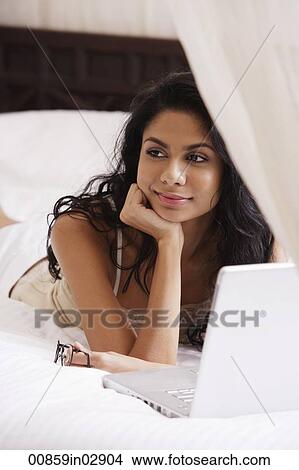 Indian woman laying on bed smiling with laptop View Large Photo Image Picture - Indian woman laying on bed smiling with laptop. Fotosearch