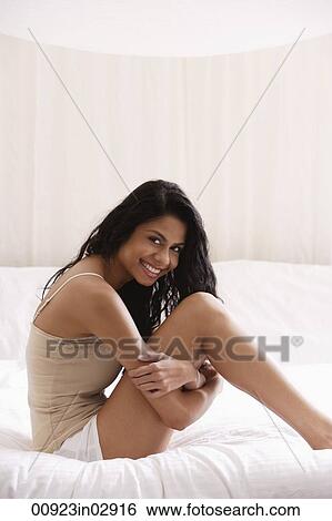 Indian woman sitting on bed holding legs. View Large Photo Image Stock Photograph - Indian woman sitting on bed holding legs.. Fotosearch