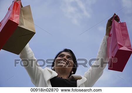 Stock Image - Indian woman smiling and holding up shopping bags. Fotosearch