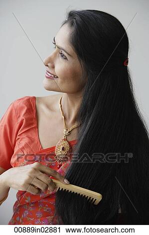 Stock Image - Indian woman smiling while combing hair. Fotosearch