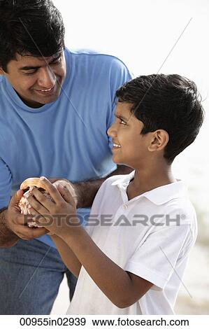 Stock Photo - Father and son holding sea shell and smiling. Fotosearch