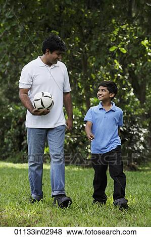 Father and son walking together in park holding ball View Large Photo Image Stock Photo - Father and son walking together in park holding ball. Fotosearch