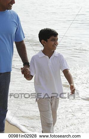 Father holding son's hand while walking on beach View Large Photo Image Stock Photo - Father holding son's hand while walking on beach. Fotosearch
