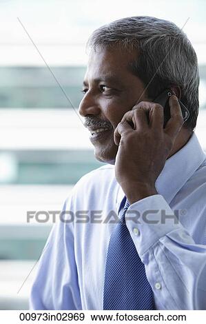 Head shot of mature Indian business man talking on phone View Large Photo Image Stock Photo - Head shot of mature Indian business man talking on phone. Fotosearch