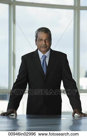 Indian business man standing at desk View Large Photo Image Stock Photograph - Indian business man standing at desk. Fotosearch