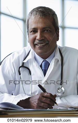 Indian doctor sitting at desk and smiling View Large Photo Image Stock Photo - Indian doctor sitting at desk and smiling. Fotosearch