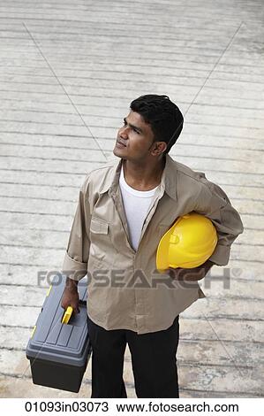 Stock Image - Man holding construction hat and tool box looking away. Fotosearch