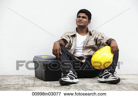man sitting on ground holding construction hat View Large Photo Image Stock Photo - man sitting on ground holding construction hat. Fotosearch