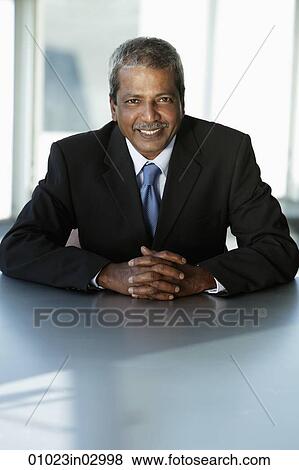 Mature Indian business man sitting at table smiling View Large Photo Image Stock Photo - Mature Indian business man sitting at table smiling. Fotosearch