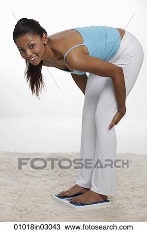 Stock Image - woman bending down looking at scale. Fotosearch