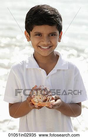 Stock Photography - Young boy holding sea shell and smiling. Fotosearch