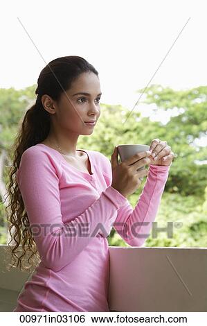 Young woman holding cup leaning on balcony View Large Photo Image Stock Photograph - Young woman holding cup leaning on balcony. Fotosearch