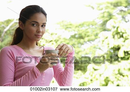 Stock Photo - Young woman holding cup looking at camera. Fotosearch