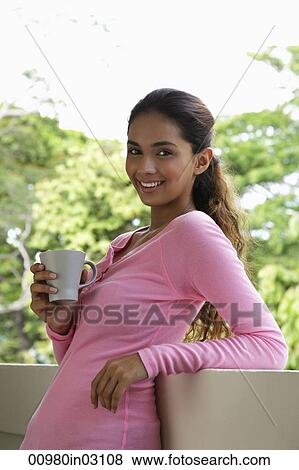 Young woman holding mug leaning on balcony View Large Photo Image Stock Photo - Young woman holding mug leaning on balcony. Fotosearch
