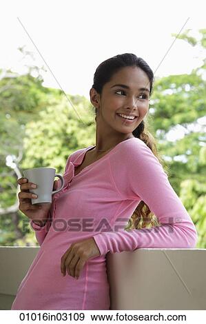 Young woman holding mug looking over shoulder View Large Photo Image Stock Photo - Young woman holding mug looking over shoulder. Fotosearch