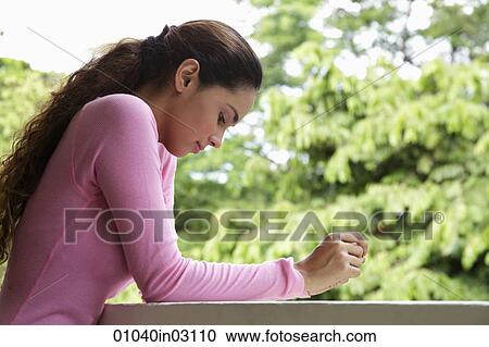 Stock Image - Young woman leaning on balcony looking down. Fotosearch