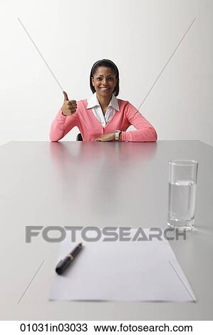 Young woman sitting at table during interview giving thumbs up sign View Large Photo Image Stock Image - Young woman sitting at table during interview giving thumbs up sign. Fotosearch