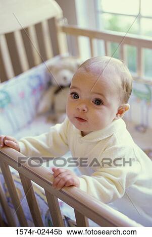Stock Image - Baby boy holding the railing of a crib. Fotosearch