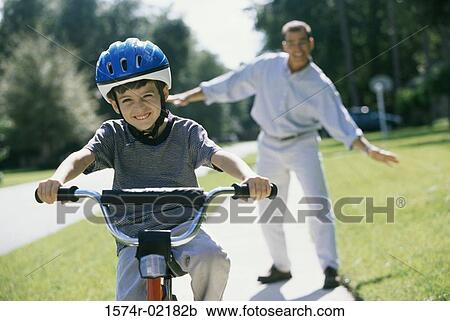 Boy cycling with his father standing behind him View Large Photo Image Stock Image - Boy cycling with his father standing behind him. Fotosearch