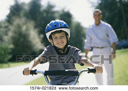 Stock Image - Boy cycling with his father standing behind him. Fotosearch