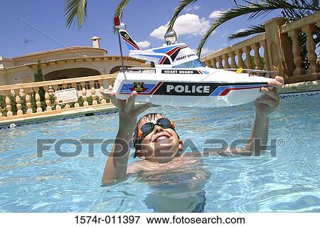 Stock Photo - Boy holding a toy boat in a swimming pool. Fotosearch