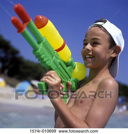 Boy holding a toy squirt gun at the beach View Large Photo Image Stock Photo - Boy holding a toy squirt gun at the beach. Fotosearch
